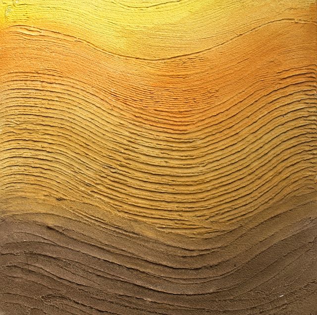 Tekstura ściany z wyraźnymi, poziomymi żłobieniami, przechodząca od jasnego żółtopomarańczowego u góry do ciemnego brązu u dołu, przypominająca warstwy ziemi lub piasku.